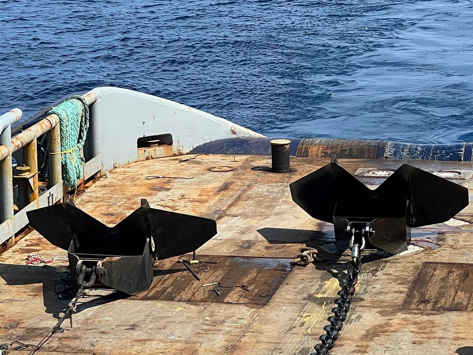 Two black fluke anchors shackled to chain on the open stern deck of a work boat at sea