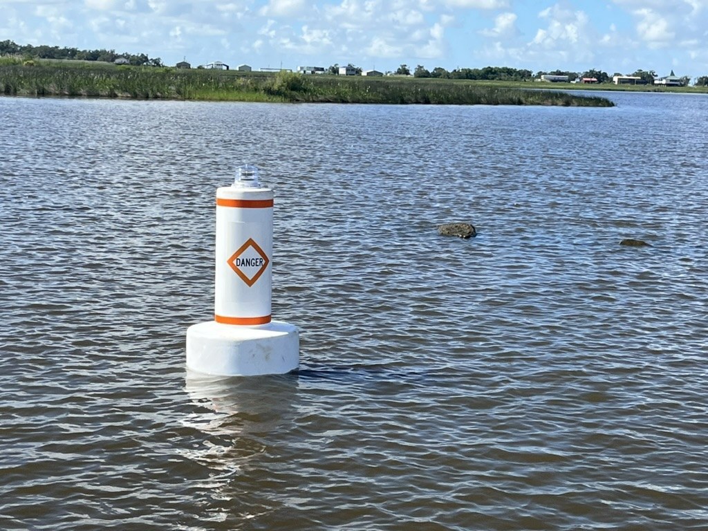 M-711LP white inland water marker buoy with orange bands and danger diamond on station in shallow marsh water